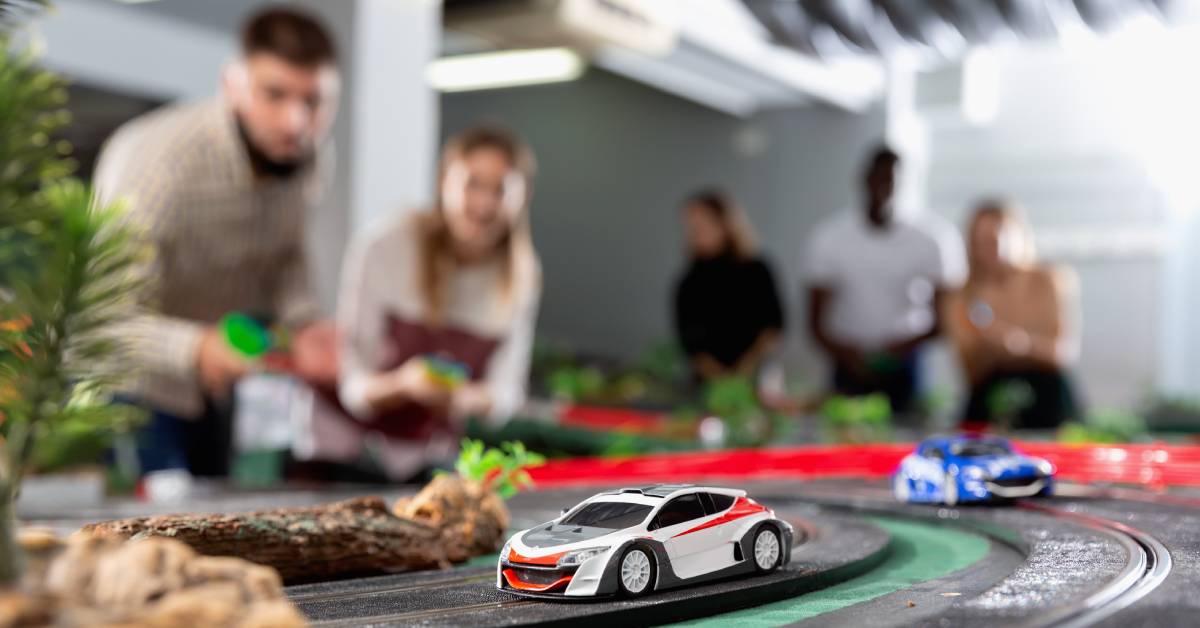 A group of people in the background, out of focus, racing slot cars on a detailed track featuring jungle-like scenery.